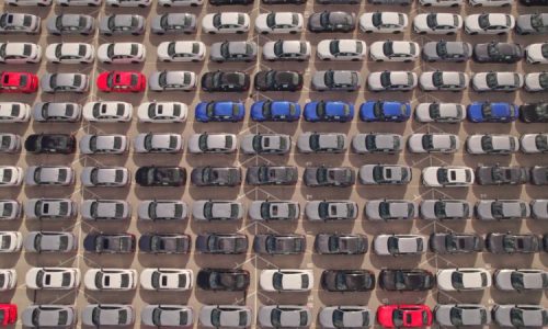 New cars located at the factory parking lot aerial view at golden hour. Car manufactory parking area for a new hybrid EV. High tech green electric vehicles sorted after industrial production conveyor.